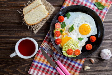Fried eggs in pan with tomato, bread, pepper and parsley on wooden background