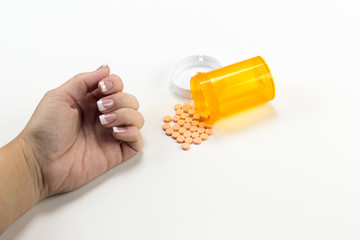 Pills spilling out of medicine bottle near womans hand possible suicide overdose posed