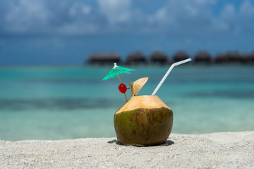 Coconut with drinking straw on beach at the sea