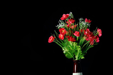 Artificial red flowers in vase on black background.