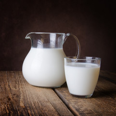 Glass jug and glass with milk on a wooden rustic background.