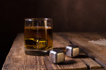 Whiskey glass with stainless steel ice cubes on wooden rustic background. Selective focus.