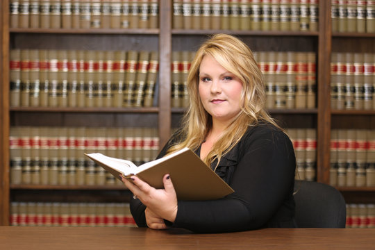 Young attractive female professional, portrait of woman lawyer in law office with law book