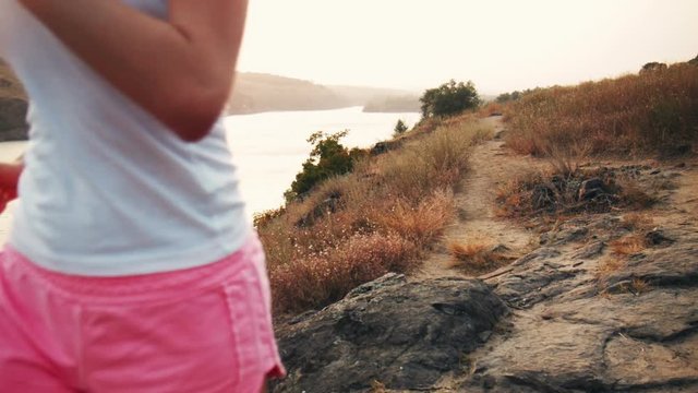 Rear view of young sportswoman in shorts and top running along river in sunlight