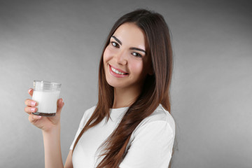 Beautiful woman with glass of milk on grey background