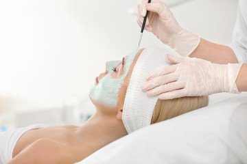 Obraz na płótnie Canvas Cosmetologist applying facial mask in beauty salon