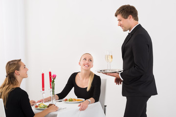 Waiter Serving Glass Of Champagne To Female Friends