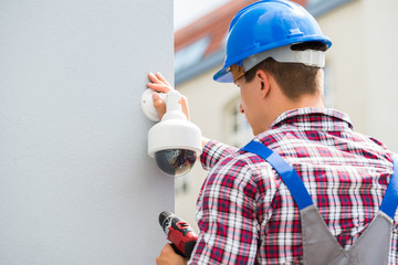Young Male Technician Installing Camera On Wall