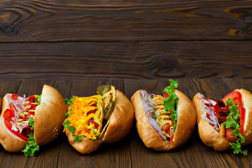 A lot of big delicious hot dogs with sauce and vegetables on wooden background. Their assorted hot dogs to gourmet with copy space for design.