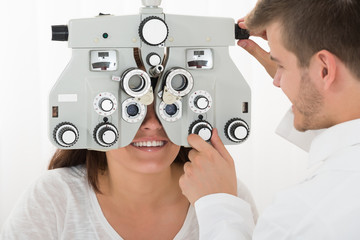 Male Optometrist Adjusting Phoropter While Examining Patient