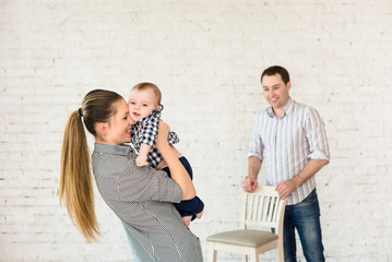 Mother, father, baby boy in light room on the white brick wall background