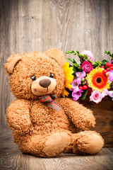 Bunch of flowers and a teddy bear on wooden background