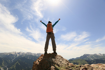 Fototapeta na wymiar cheering young woman backpacker open arms on mountain peak cliff