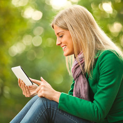 Happy woman is using digital tablet in park.