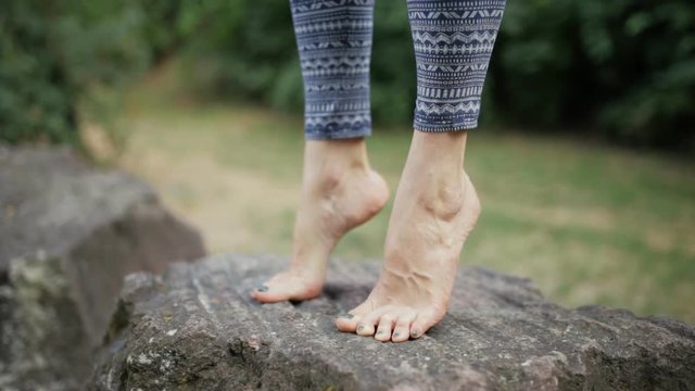 Woman practicing yoga on big stone. Legs close up.
