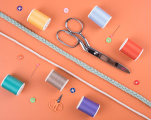 closeup needles, thread spool, scissors, button on orange wooden