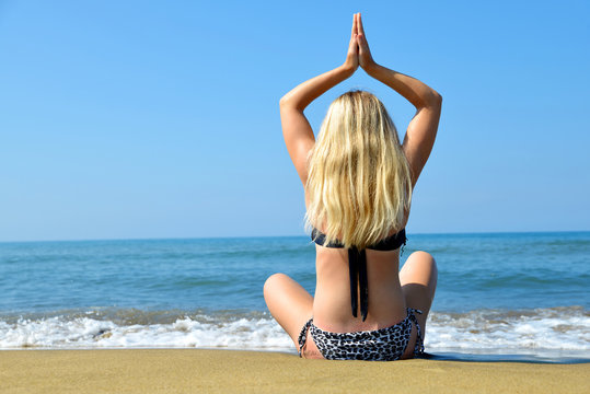 Young woman practicing yoga on sandy beach