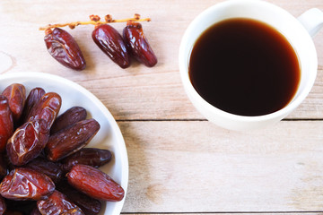 Top view of pile of dried date fruit with black coffee on a wooden table.