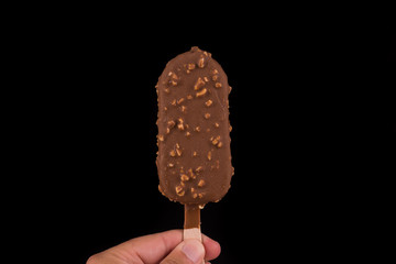 Fingers holding vanilla ice cream covered with chocolate and peanuts on black background