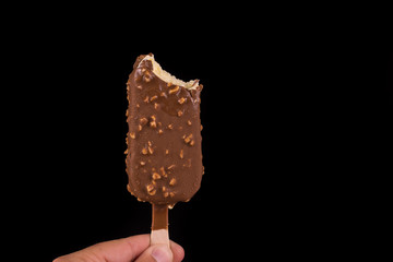 Vanilla ice cream covered with chocolate and peanuts on black background