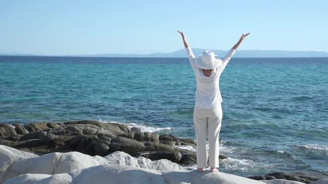 Woman with hands up standing on the rock near the sea