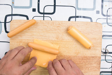 Hands wrap sausage with cheese