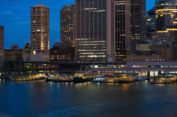Fototapeta na wymiar Circular Quay railway, train station and ferry wharfs with Sydney Central Business District cityscape skyscrapers at the background. Night shot, long exposure, copy space