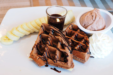 Delicious waffle with chocolate syrup, banana, ice scream and whip cream. Selective focus.