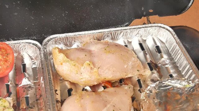 Healthy grilling of chicken steak  in aluminum case on gas stone grill. Cooking of white pepper, garlic, tomatoes , champignons, sausages  and potatoes  wrapped in aluminum foil.