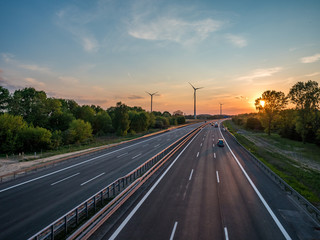 sunset over a highway, wind turbines in the background