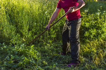 man mows the grass using a scythe in a field lit by the sun