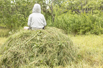 child sits on haystack and enjoy the warm a summer eveningon the background of green of bushes and fence