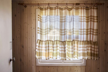 Rustic window from inside the house, closed by curtains, through which visible nature, the neighboring houses and the sky.