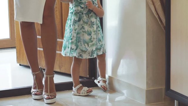 Pretty woman with little girl stand in door, go and smiling. Slowly
