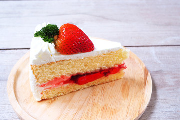 Close up of Strawberry cake with fresh strawberry topping in a wooden plate.