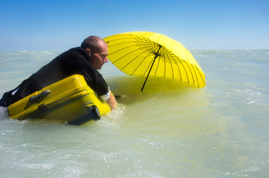 Man swims on a suitcase with an umbrella on the sea