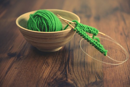 knitting with green wool on wooden table
