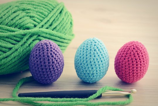 crocheting easter eggs with blue pink green. wooden table backgr
