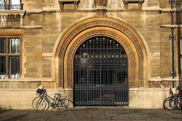 Fototapeta na wymiar Parked bikes leaning against historic stone building of Gonville And Caius College, Cambridge, by ornamental iron gate.
