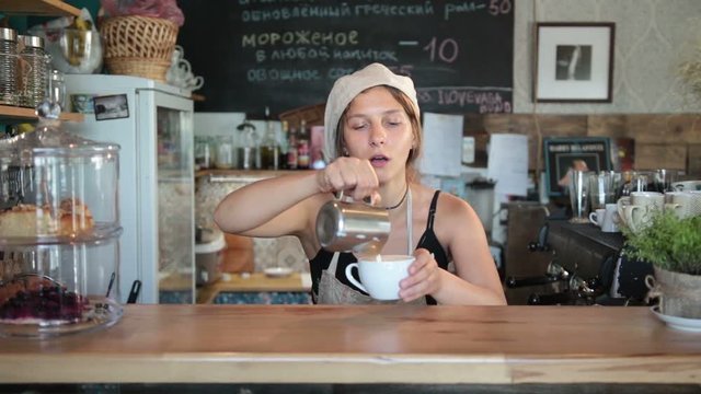 Cute female barista pouring milk into coffee cup