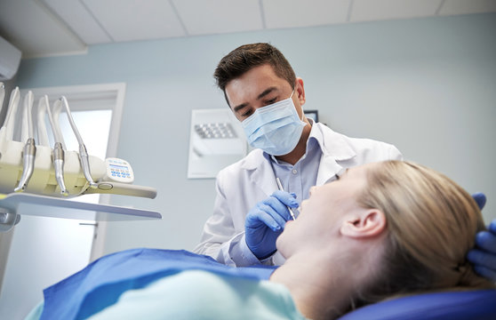male dentist in mask checking female patient teeth