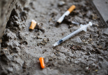 close up of syringe and smoked cigarette on ground