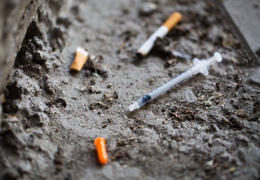 close up of syringe and smoked cigarette on ground