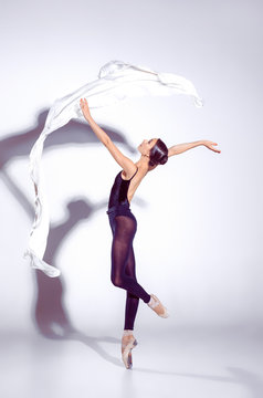 Ballerina in black outfit posing on toes, studio background.