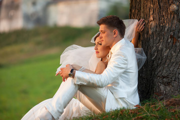 Bride's veil blows up while she sits with a groom on the grass