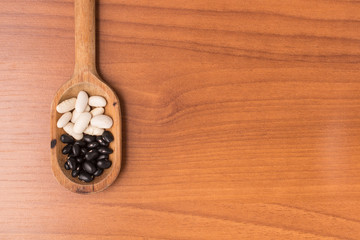 White and black Raw beans into a spoon over a wooden table.