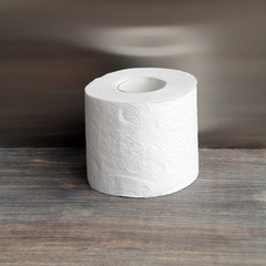 Roll of toilet paper on wooden table against steel background
