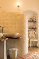 Elegant tiled bathroom in natural tones with design sinks and faucets, curved opalescent tile wall, niche with shelves
