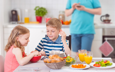 Two happy children eating breakfast during father works
