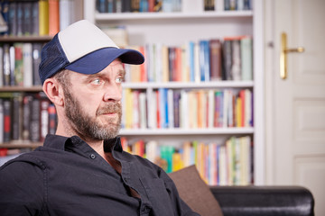 Man with beard and baseball cap sitting in a library